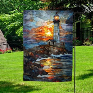 May include: A decorative garden flag featuring a stained-glass style image of a lighthouse at sunset. The lighthouse is white with a black top, set on a rocky shore with waves. The sky is a vibrant mix of orange, yellow, and blue.