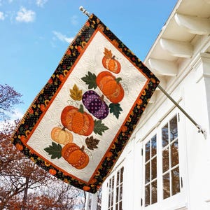 May include: A rectangular outdoor flag featuring a vertical stack of five patterned pumpkins in shades of orange, yellow, and purple, accented with green leaves. The flag has a black border with sunflowers and is mounted on a metal pole.