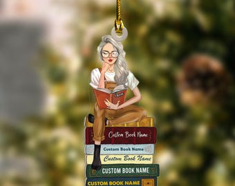 May include: Ornament featuring a woman with gray hair and glasses reading a book while sitting on a stack of books. The books have the text "Custom Book Name" on them. The ornament is suspended by a gold string.