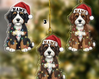 May include: Three acrylic dog ornaments, each featuring a different breed, wearing a Santa hat with the word "NAME" and a string of colorful Christmas lights. The ornaments are suspended by gold cords.
