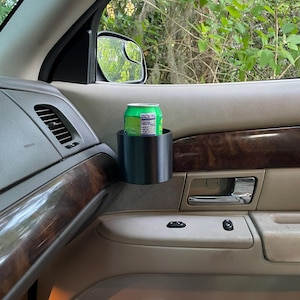 Puede incluir: Un portavasos de coche negro con una lata verde de Mountain Dew en su interior. El portavasos está fijado al panel de la puerta del coche.