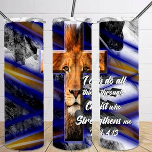 May include: A white tumbler with a blue and gold striped background. The tumbler features a lion's face with a cross behind it. The text "I can do all things through Christ who strengthens me. Phil 4:13" is printed on the tumbler.