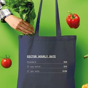 May include: An Oxford navy tote bag featuring white text that reads: EDITOR HOURLY RATE, Standard $50, If you watch $75, If you help $100. The bag is surrounded by floating fresh produce including an orange bell pepper, celery, a red tomato, a red bell pepper, an artichoke, and a small pumpkin.
