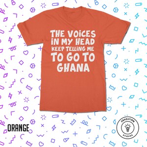 May include: Orange t-shirt with white text that reads "The Voices in My Head Keep Telling Me To Go To Ghana". The shirt is on a white background with a colorful pattern.