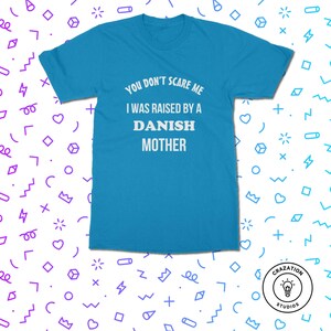 Może przedstawiać: Turkusowa koszulka z białym napisem: "YOU DON'T SCARE ME I WAS RAISED BY A DANISH MOTHER". Koszulka ma kr&oacute;tkie rękawy i okrągły dekolt. Logo Crazation Studios znajduje się w prawym dolnym rogu.