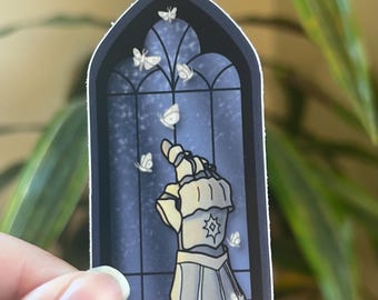 May include: A sticker featuring a stylized illustration of a hand in armor reaching towards butterflies. The background is a dark blue stained glass window with butterflies. The sticker has a white border.