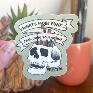 May include: A sticker with a skull design, featuring the text "WHAT'S MORE PUNK THAN USING YOUR BRAIN?" and "REJECT AI." The skull's open top is filled with pencils and paintbrushes. The sticker has a light green background.