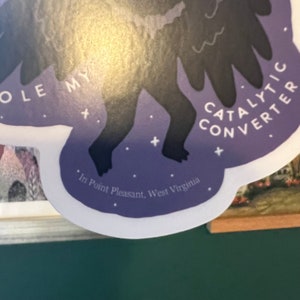 May include: Purple sticker with a black silhouette of a creature with wings. The text "Catalytic Converter" is written on the sticker. The text "In Point Pleasant, West Virginia" is written at the bottom of the sticker.