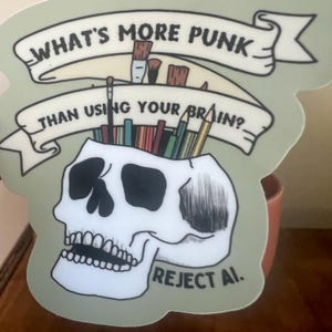 May include: A sticker with a skull design, pencils, and paintbrushes. The sticker has the text "WHAT'S MORE PUNK THAN USING YOUR BRAIN?" and "REJECT AI." The sticker is light green with a white skull.