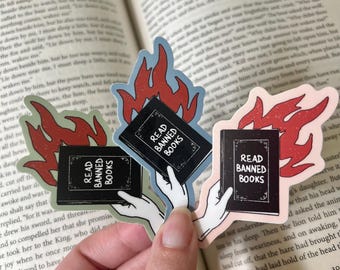 May include: Three sticker designs featuring a hand holding a book engulfed in flames. Each sticker reads "Read Banned Books".