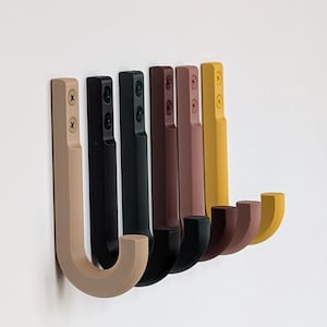 May include: Six wall hooks in different colors: beige, black, dark green, brown, maroon, and yellow. The hooks are made of a smooth, rounded material and have a J-shape.