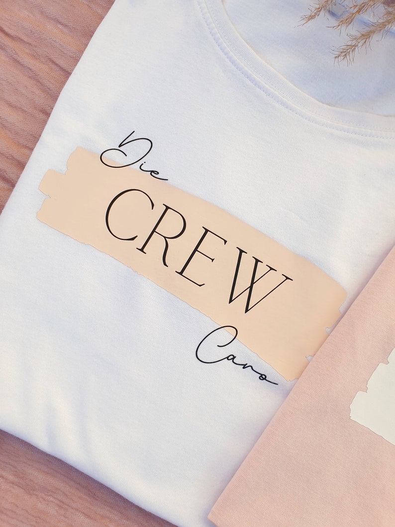 May include: White t-shirt with a peach-coloured label that says "Die Crew Caro" in black script.