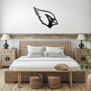 May include: A wooden bed frame with a white duvet and pillows. The bed has a wooden headboard and footboard. There is a wooden bench at the foot of the bed and two wicker baskets on the floor. A black metal cardinal bird silhouette is mounted on the wall above the bed.
