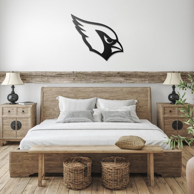 May include: A wooden bed frame with a white duvet and pillows. The bed has a wooden headboard and footboard. There is a wooden bench at the foot of the bed and two wicker baskets on the floor. A black metal cardinal bird silhouette is mounted on the wall above the bed.
