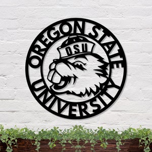 May include: Black and white metal wall art featuring the Oregon State University logo. The logo is a beaver wearing a hat with the letters "OSU" on it. The words "Oregon State University" are written in a circle around the beaver.