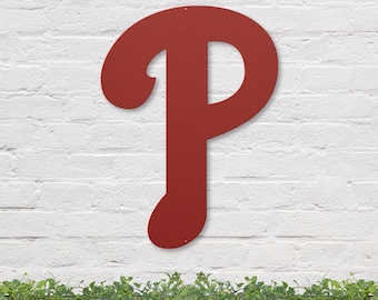 May include: A large, red metal letter "P" with a stylized font, mounted on a white brick wall. The letter is a popular symbol for the Philadelphia Phillies baseball team.