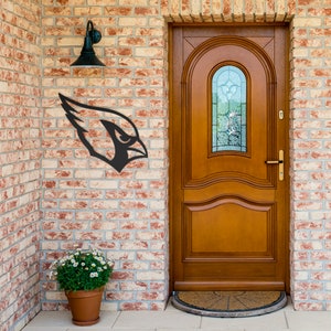 May include: A black metal cardinal bird head silhouette wall decor mounted on a brick wall next to a wooden door with a glass window.