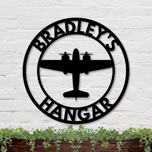 May include: Black metal circle sign with the text "Bradley's Hangar" and a silhouette of a vintage airplane in the center.