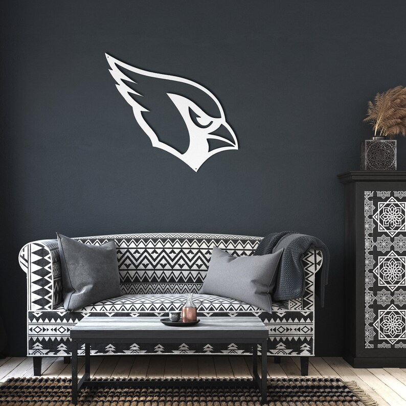 May include: White metal silhouette of a cardinal bird head, mounted on a dark gray wall above a black and white patterned sofa with gray throw pillows. The sofa is in front of a black cabinet with a geometric pattern.