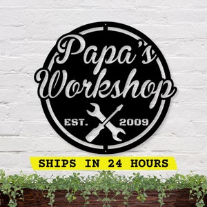May include: Black and white metal sign with the text "Papa's Workshop" in a script font. The sign also includes the text "EST. 2009" and a pair of crossed wrenches.