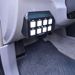 May include: A black switch panel with eight buttons and a power button labeled "VOSWITCH" mounted in a car's interior.