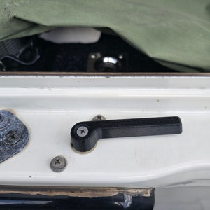 May include: A black plastic handle with a screw in the center, attached to a white surface with two screws.