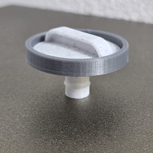 May include: A gray 3D printed plastic cap with a white handle on top. The cap has a threaded opening on the bottom.