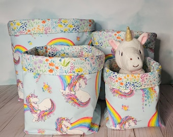 Peut inclure: Trois paniers de rangement en tissu bleu et blanc avec un motif arc-en-ciel et licorne. Les paniers sont doublés d'un tissu à imprimé floral. Le plus grand panier contient un jouet en peluche licorne blanche.