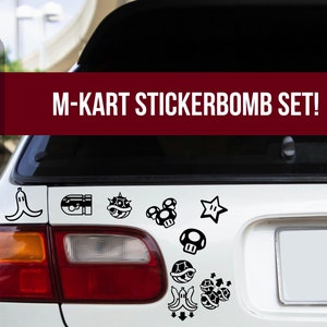 Può includere: Un'auto bianca con un lunotto posteriore nero e una varietà di adesivi Mario Kart in bianco e nero sul retro. Gli adesivi includono una buccia di banana, un guscio, una stella e un fungo.