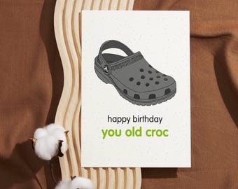 Könnte beinhalten: Eine Geburtstagskarte mit einer Cartoon-Illustration eines grauen Clogs. Die Karte lautet "Happy Birthday you old croc".