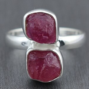 May include: A silver ring with two pink ruby stones set in the band. The stones are rough and have a natural, unpolished look.