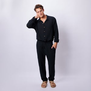 May include: Black linen shirt with wooden buttons and matching drawstring pants. The outfit is paired with tan sandals. The shirt has long sleeves and a classic collar. The pants have a relaxed fit and a drawstring waist.