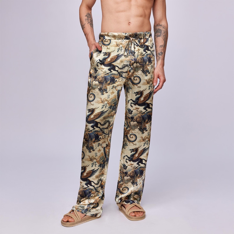 Puede incluir: Pantalones de pijama color crema con un estampado repetido de criaturas m&iacute;ticas en tonos negros, azules y marrones. Los pantalones tienen cintura con cord&oacute;n y un corte holgado. La tela tiene un ligero brillo.