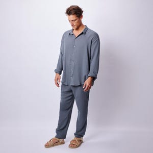 May include: A two-piece set of casual wear in a muted blue-grey color. The set includes a long-sleeved button-down shirt and matching pants. The person is wearing beige sandals.