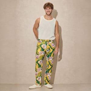 May include: A cream ribbed vest top and yellow trousers with a floral pattern of white and pink flowers and green leaves. The trousers have a yellow background. The outfit is completed with white shoes.