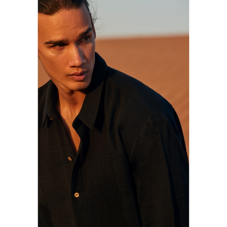 May include: A black button-down shirt with a classic collar and long sleeves. The shirt has two visible wooden buttons. The background is a desert landscape with warm, earthy tones.