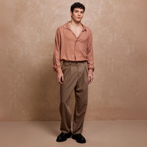 May include: A person wearing a brown patterned long-sleeve shirt with a collared neckline and a pair of brown pants.