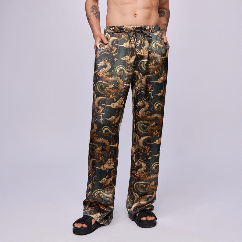 May include: Loose-fitting pajama pants with a dragon pattern in shades of gold and brown on a dark green background. The pants have a drawstring waist and pockets. The fabric has a slight sheen.