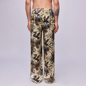 Puede incluir: Pantalones de pijama color crema con un estampado repetido de criaturas m&iacute;ticas en tonos azules, marrones y negros. Los pantalones tienen un corte holgado y una cintura c&oacute;moda. La tela tiene un ligero brillo.
