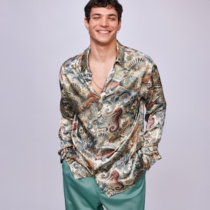 Puede incluir: Una camisa de manga larga con botones y un estampado abstracto colorido de vida marina y conchas. La camisa está hecha de una tela sedosa y tiene un corte holgado.