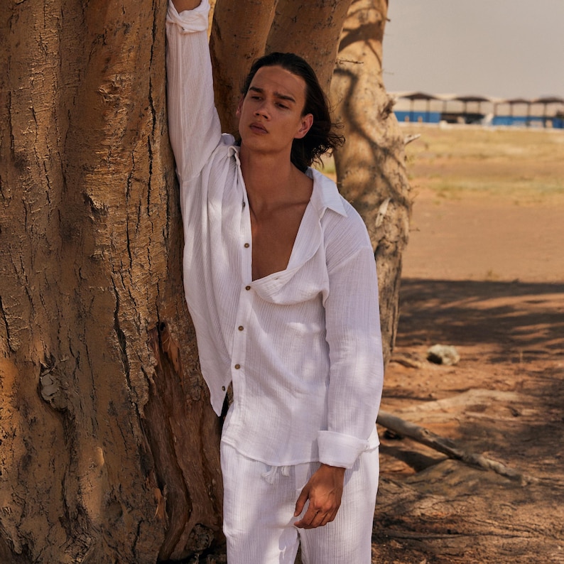 Peut inclure: Une chemise en lin blanche et un pantalon assorti. La chemise &agrave; manches longues est d&eacute;boutonn&eacute;e au niveau de la poitrine. Le mod&egrave;le est appuy&eacute; contre un tronc d'arbre. Le fond est un paysage d&eacute;sertique.