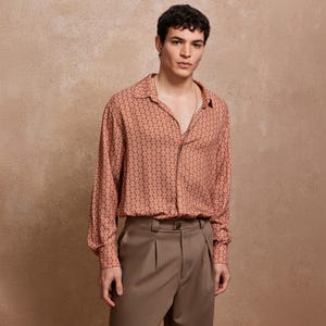 May include: A man wearing a long-sleeved, orange and white patterned shirt with a collared neckline. He is wearing brown pants.
