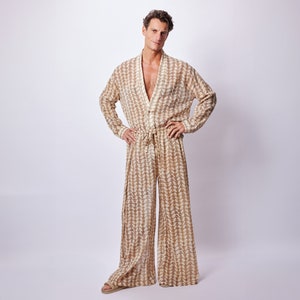 Op de afbeelding: Een persoon draagt een lange mouwen, beige jumpsuit met een bruin geometrisch patroon. De jumpsuit heeft een V-hals en een trekkoord taille.