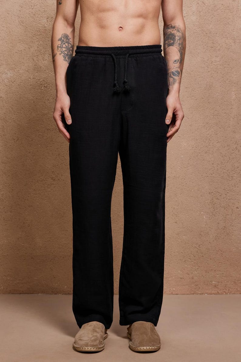 May include: Black drawstring pants with a relaxed fit. The pants have a visible drawstring at the waist and a loose, straight leg. The fabric appears to have a subtle texture. The pants are paired with light brown suede shoes.