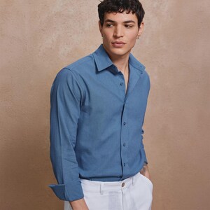 May include: A blue long-sleeve button-down shirt with a classic collar. The shirt is paired with white pants. The shirt's sleeves are cuffed, and the fabric appears to be a lightweight material.
