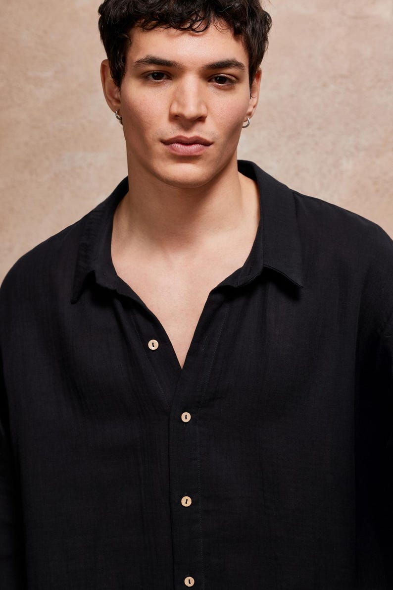May include: Black button-down shirt with a classic collar. The shirt has a relaxed fit and is made of a lightweight fabric. The buttons are a light beige color. The shirt is a solid black color.