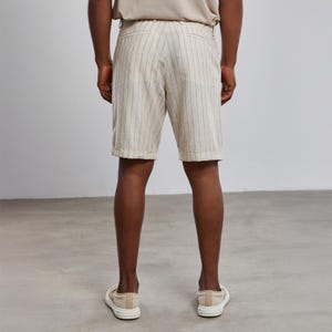 May include: White linen shorts with thin black vertical stripes. The shorts have a button and zipper closure and belt loops.