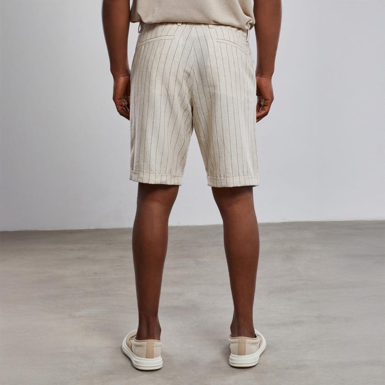 May include: White linen shorts with thin black vertical stripes. The shorts have a button and zipper closure and belt loops.