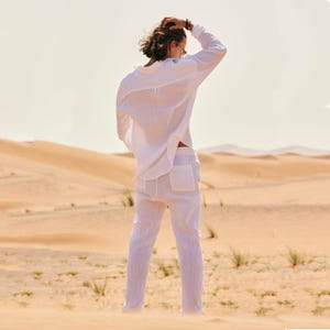 May include: White linen shirt and pants set. The long-sleeved shirt has a button-down front and a relaxed fit. The pants have a drawstring waist and pockets. The outfit is lightweight and suitable for warm weather.