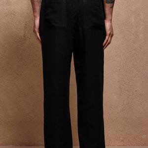 May include: Black linen pants with a relaxed fit, featuring two back pockets and a drawstring waist. The pants have a wide leg design and are made of a lightweight fabric, suitable for casual wear. The pants are shown from the back.